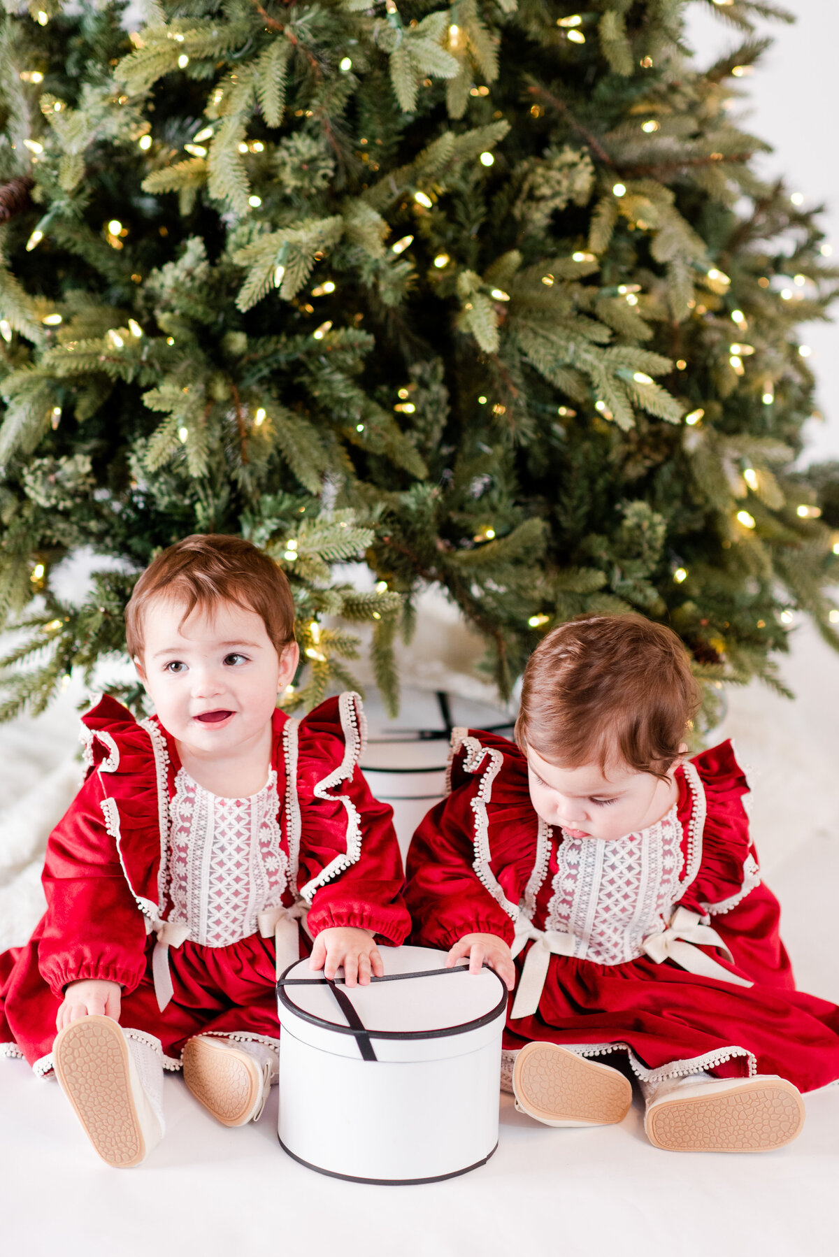 twin girls dressed in traditional Christmas outfits in front of the Christmas tree by Miami Christmas Mini Session Photographers