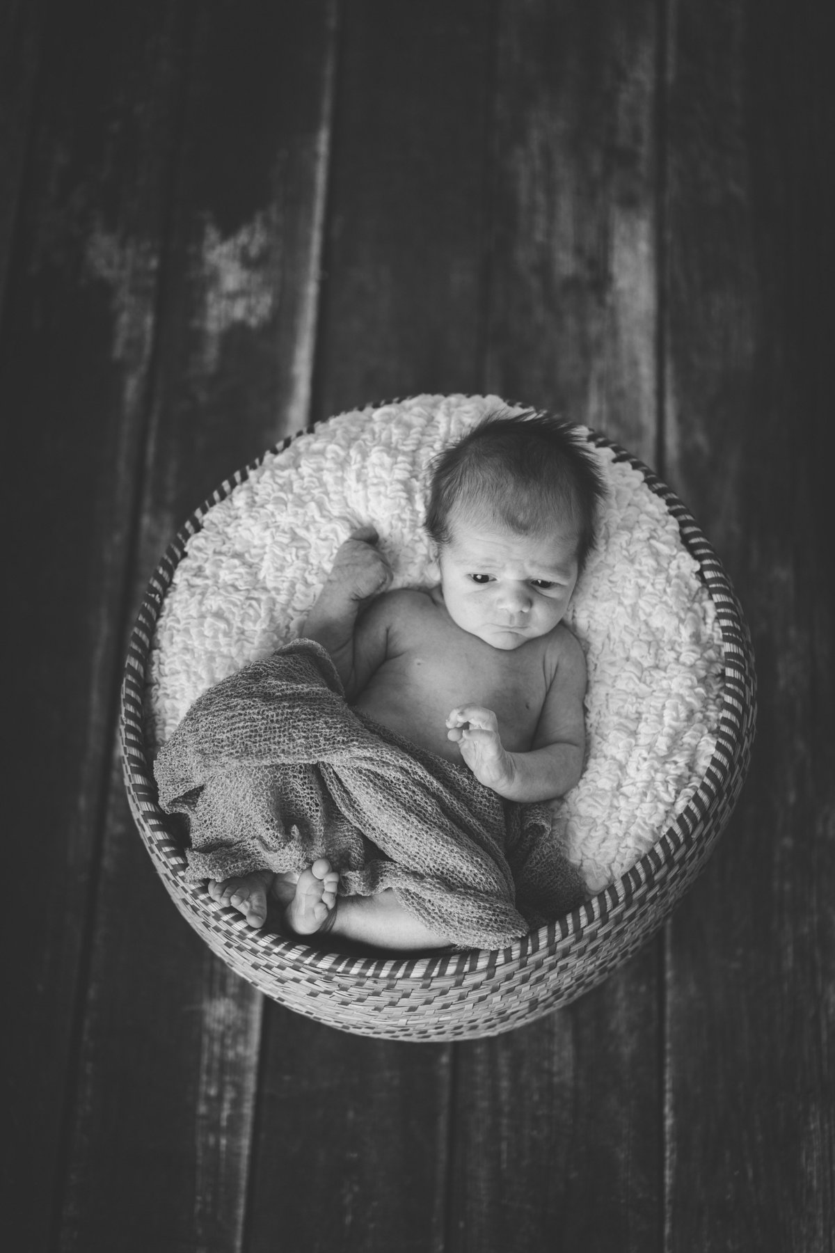 Black and white photo of newborn baby in a basket on wooden floor in San Antonio photography studio.
