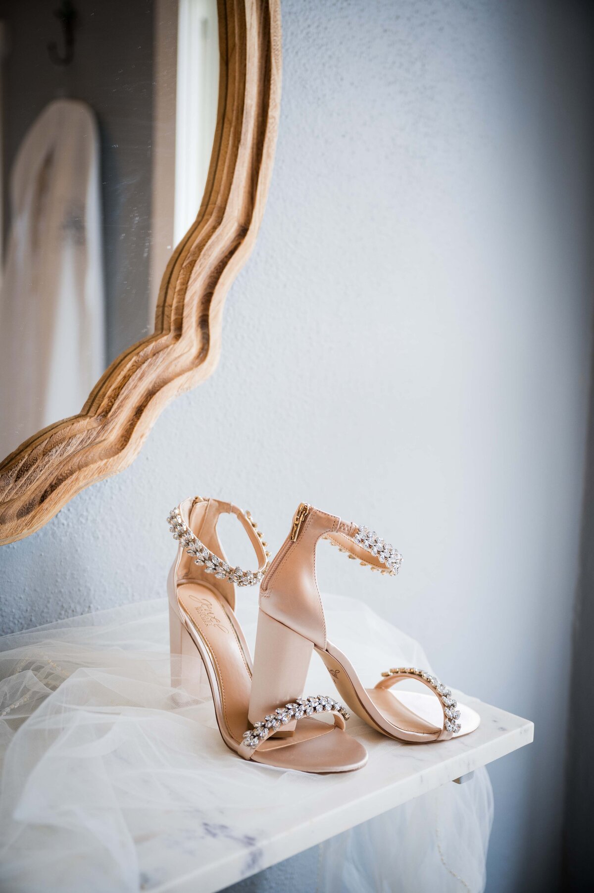 A pair of ornate wedding shoes sitting on a marble table with an ornate mirror in the background.