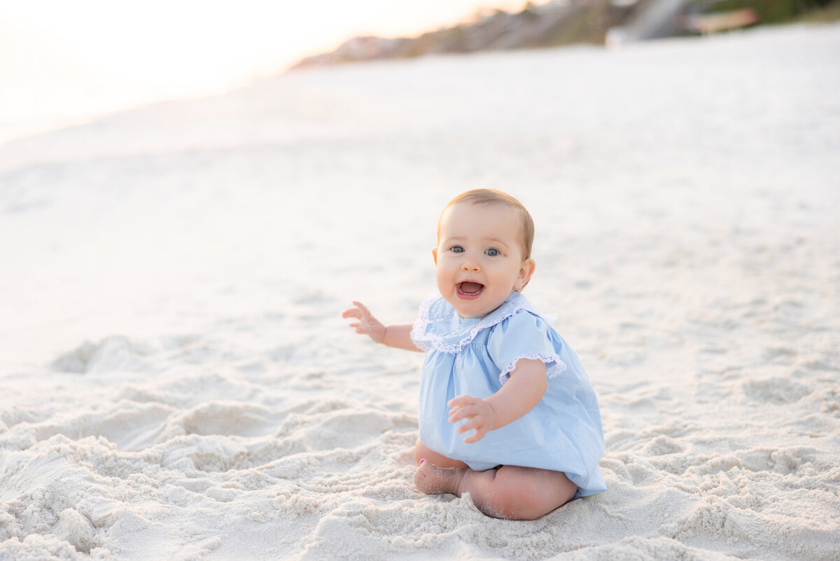 A baby smiling and sitting in the sand at Alys Beach.