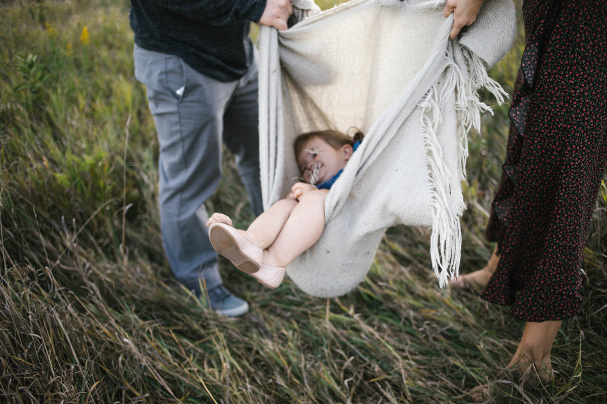 Little girl laying in a blanket swing with her parents