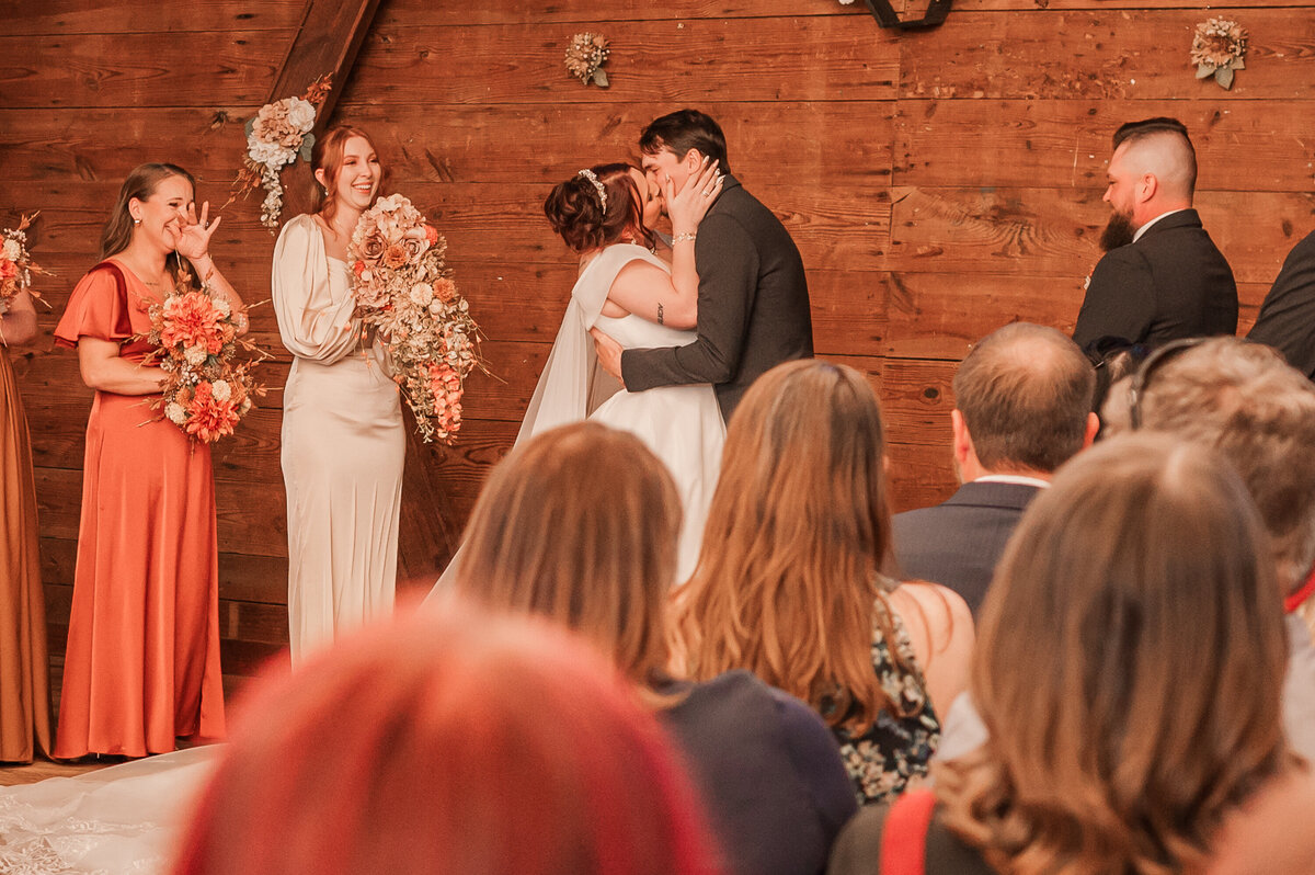 A bride and groom kissing at the wedding ceremony at The Peanut Warehouse while enjoying their Raleigh wedding photos 