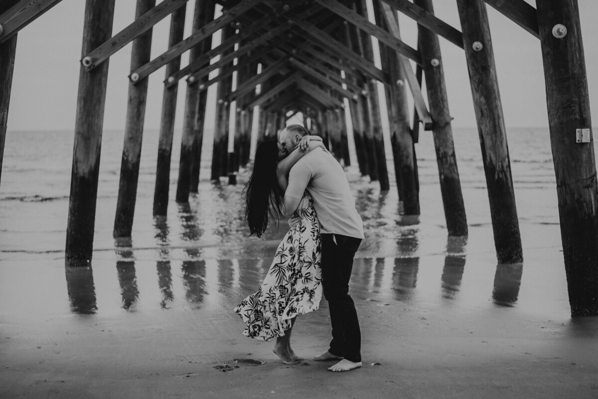 A couple kissing under a pier