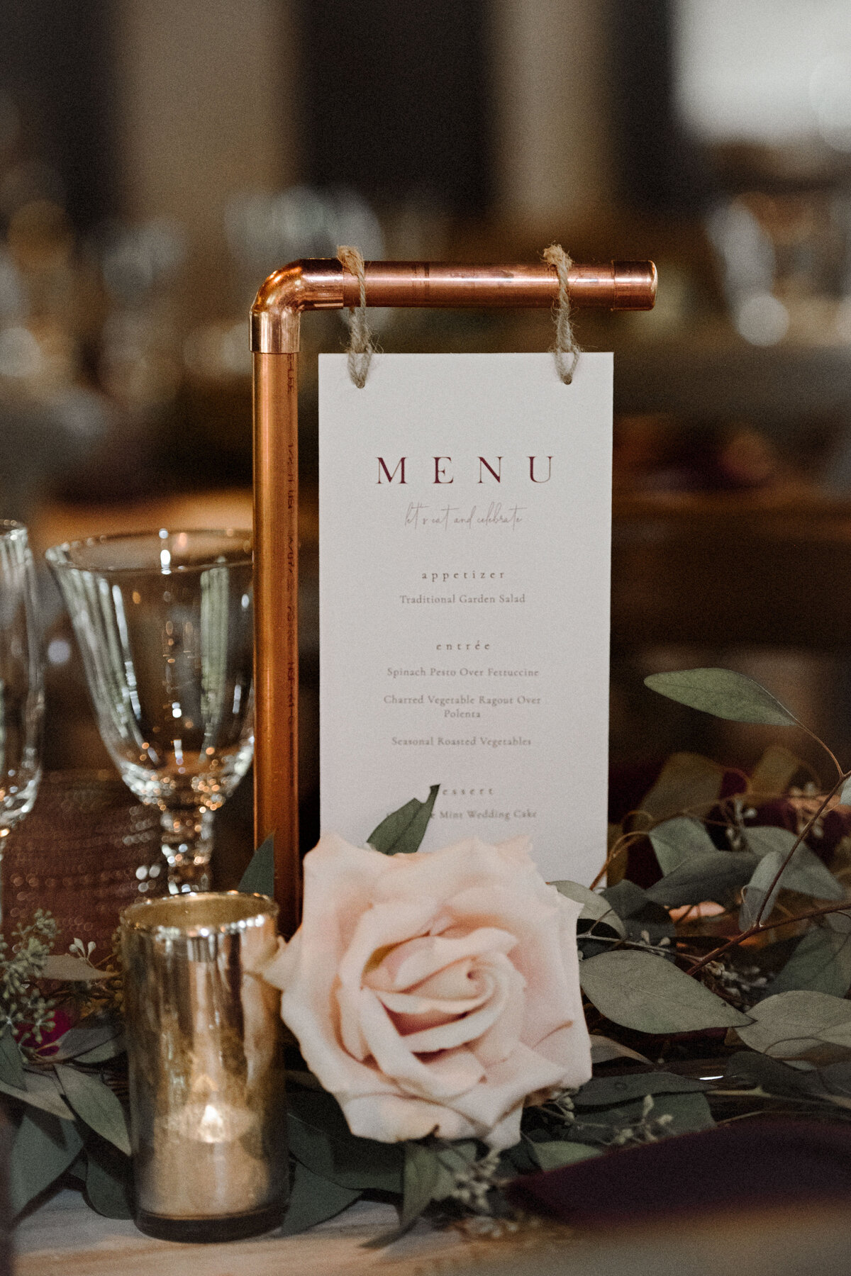 A copper pipe holdin a pink wedding menu