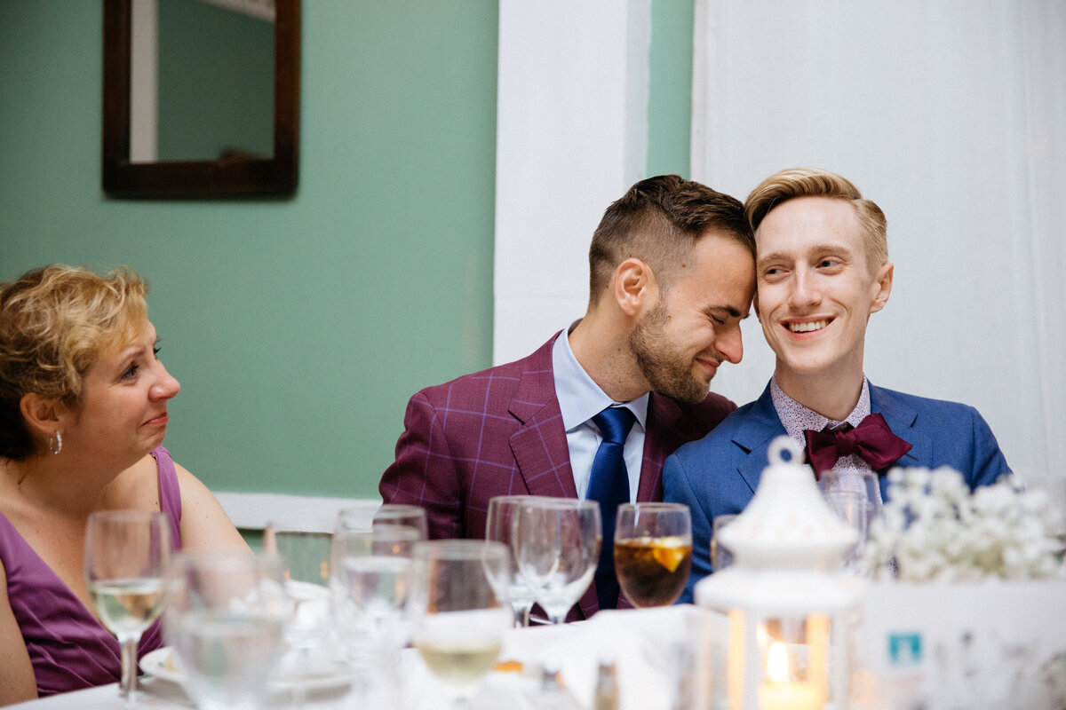 A groom resting his head on his partner's while they are sitting.