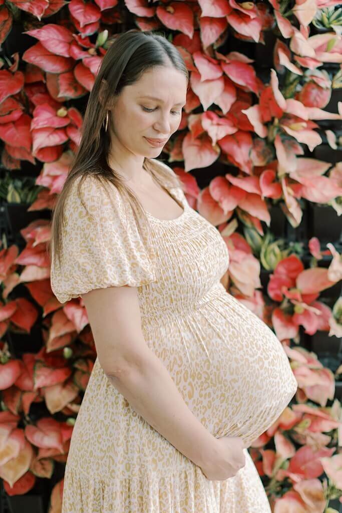 Mommy cradling her belly in a floral maternity sundress with a flower backdrop.