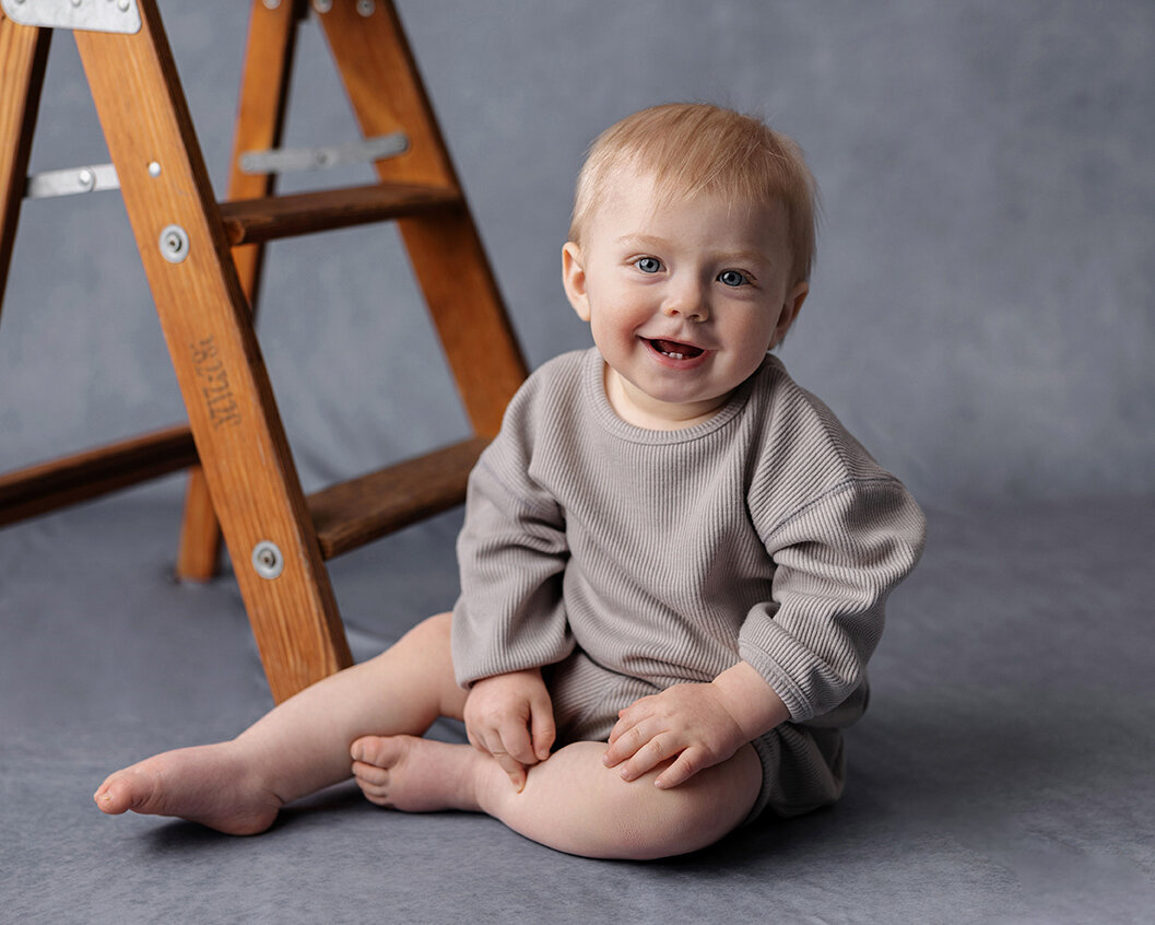 Pittsburgh photographer poses Baby siting next to a small ladder smiling for pictures.