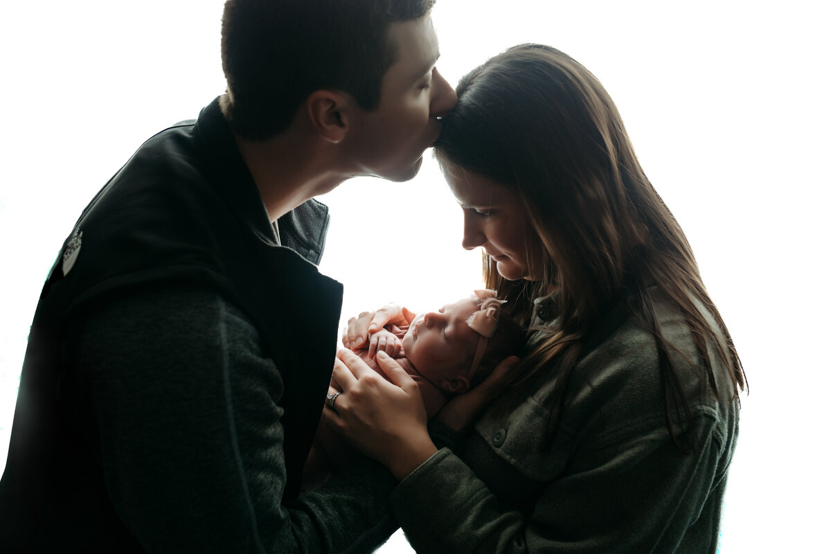 Dad kissing mother's forehead while holding newborn baby.