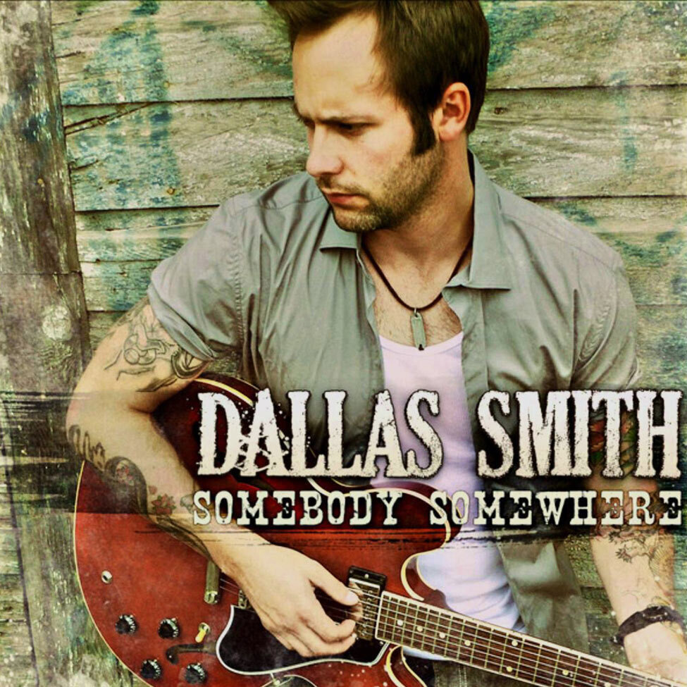 Single Cover Title Somebody Somewhere Artist Dallas Smith standing in front of weathered blue wood wall strumming orange guitar