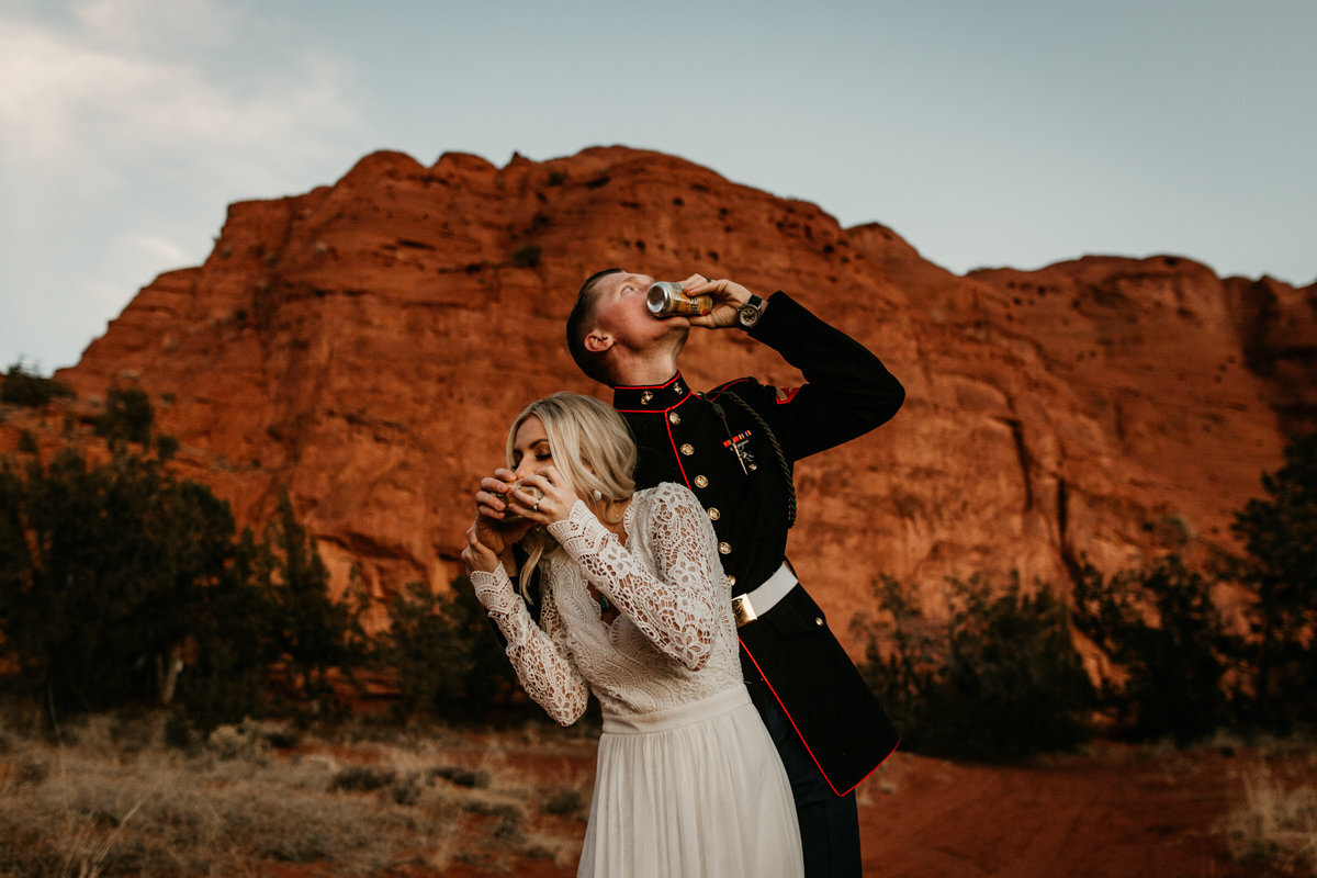 bride and groom shot gunning beer in front of red rock mountains