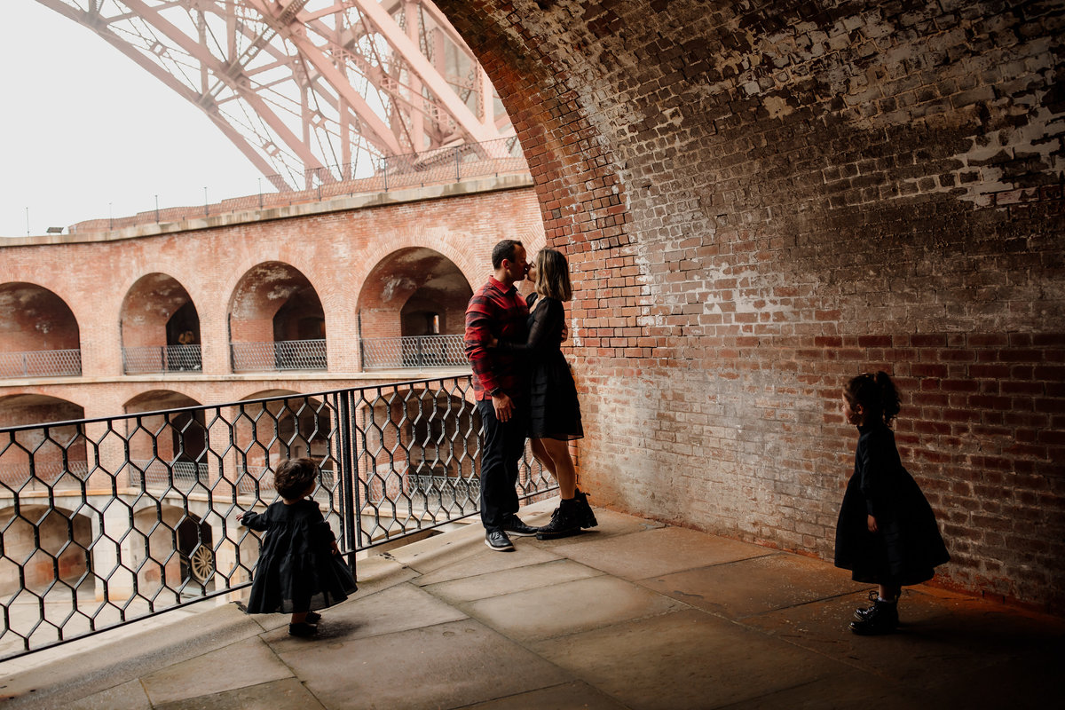 Lifestyle photo of parents kissing and kids looking at them at Fort Point SF