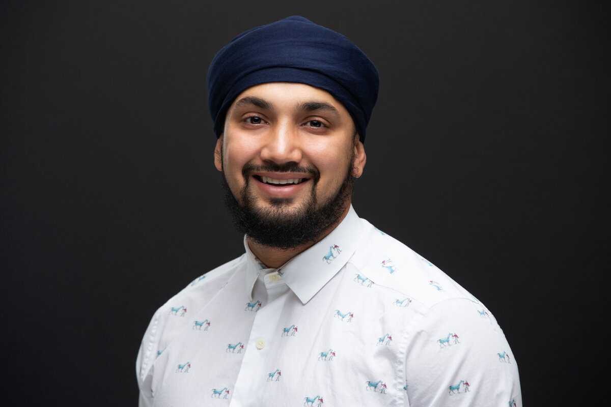 An Indian man in a blue Turban and white shirt poses for a headshot on a dark grey background for Janel Lee Photography studios in Cincinnati Ohio