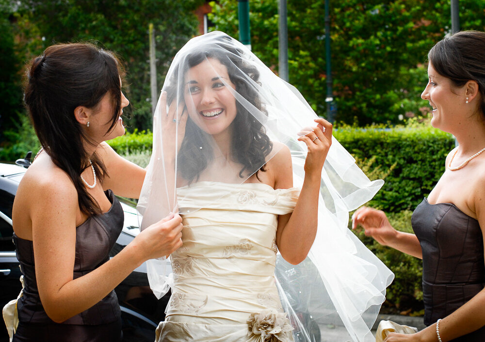brunette bride wearing a veil over her face and balcony style wedding dress being helped by her bridesmaids wearing chocolate brown, sleeveless dresses