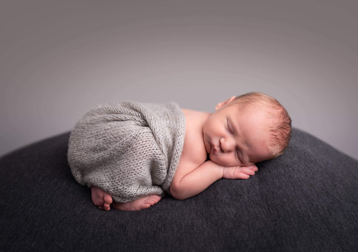 A newborn baby boy sleeps on a gray blanket