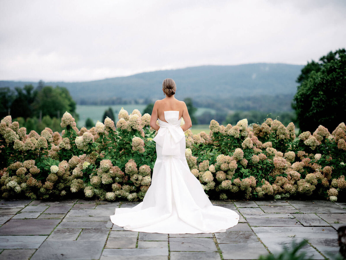 The bride is standing in a beautiful garden looking through the rolling hills at The Lion Rock Farm, Sharon, CT. Image by Jenny Fu Studio