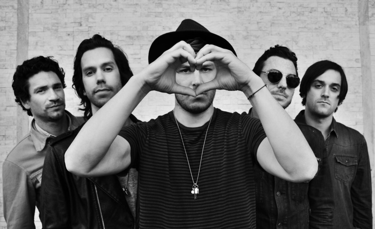 Music group portrait Terraplane Sun black and white singer holding hands in heart shape in front  of face against white brick wall
