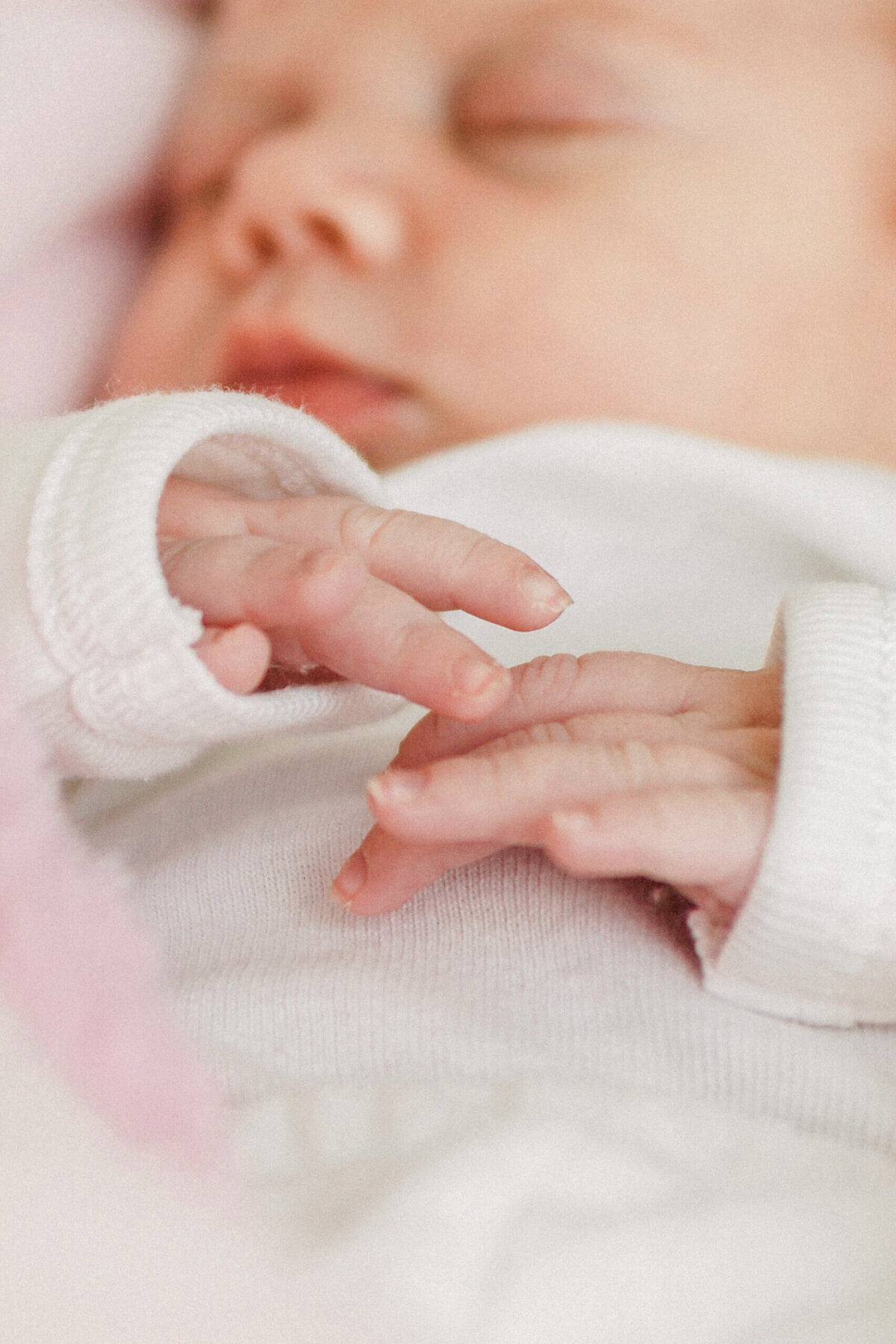 Close up photo of newborn baby hands and fingers  with her face blurred in the background.