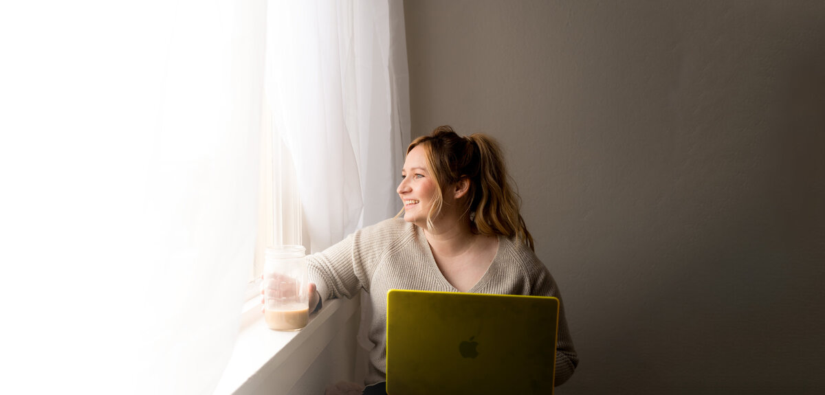 showit website designer looks out window with iced coffee and macbook pro