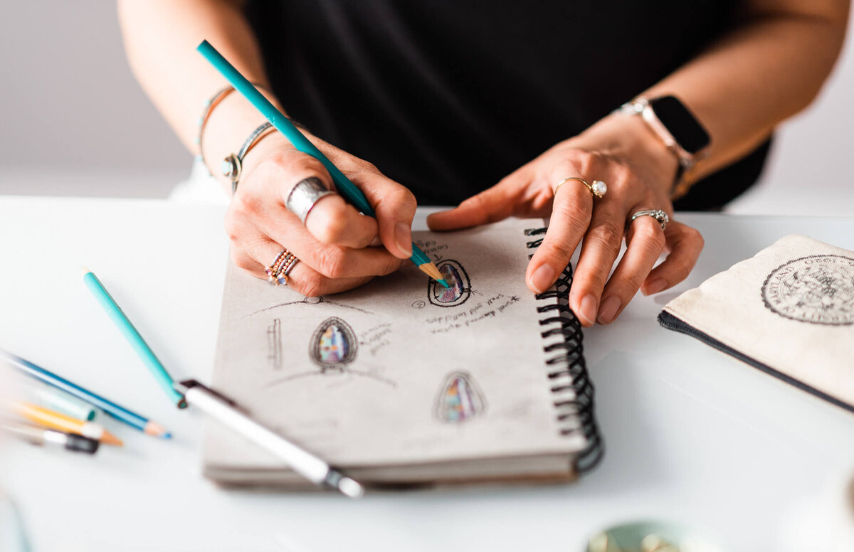 jeweler sketching a design with a teal colored pencil during her brand session with a Northern VA brand photographer