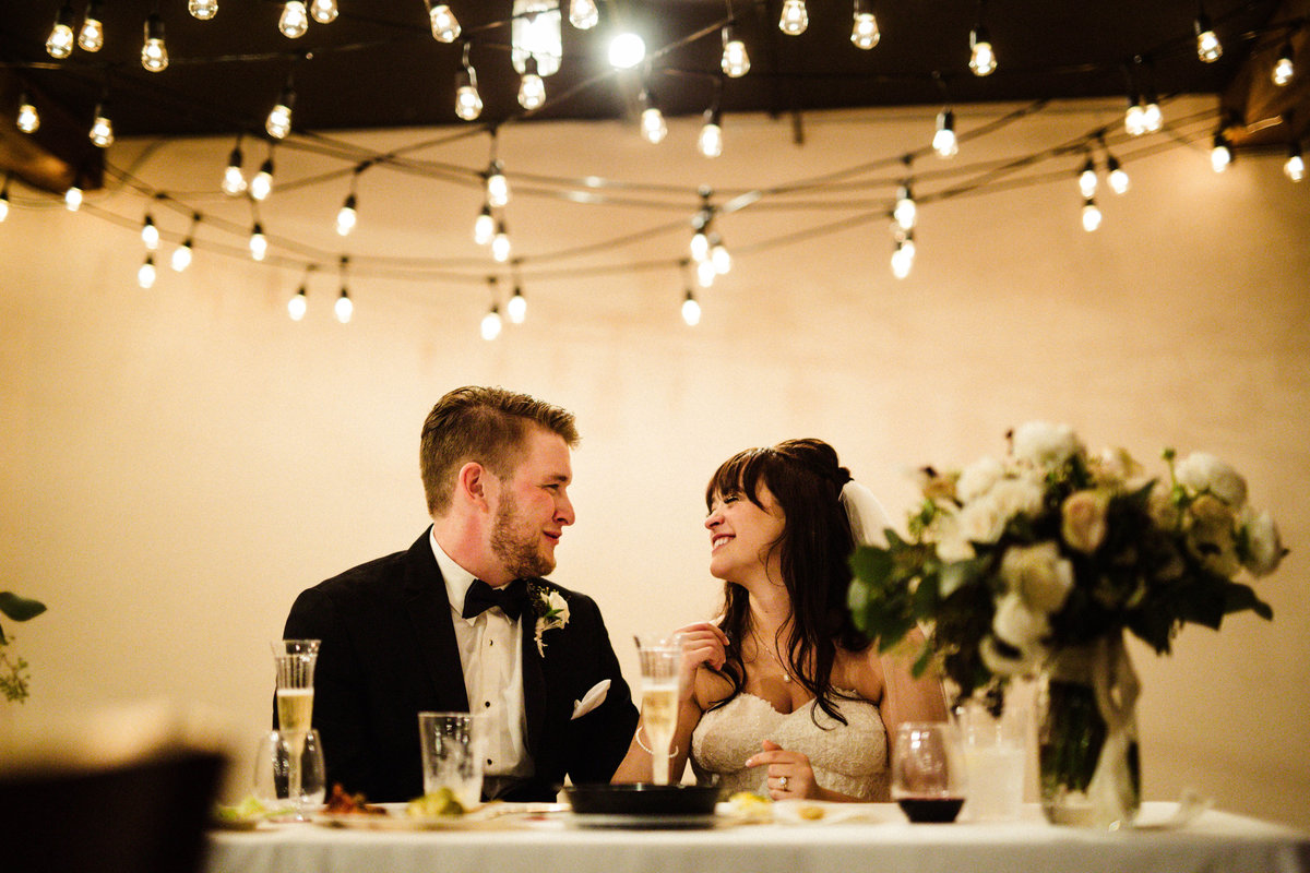 bride and groom smile at each other with twinkle lights overhead