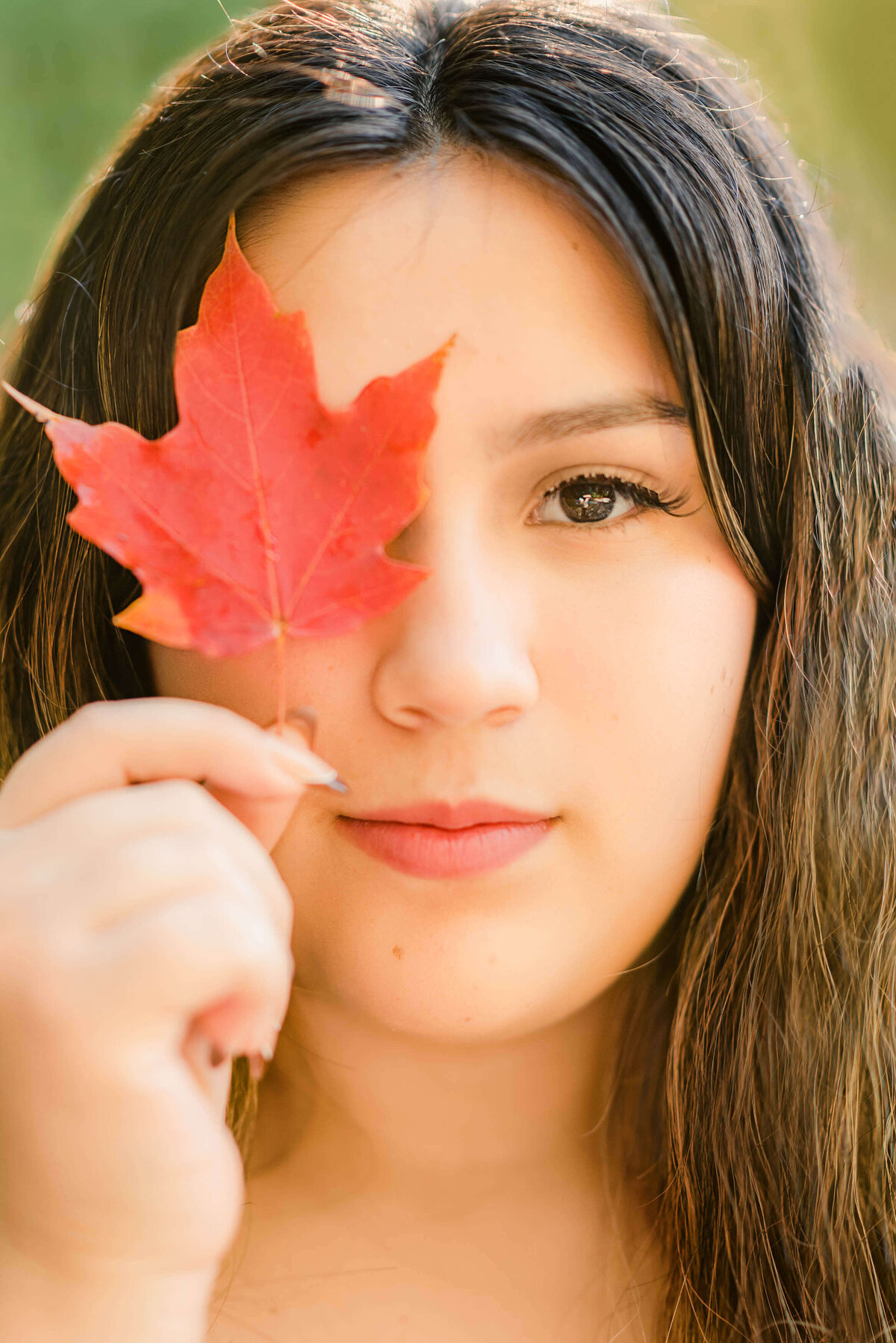 High school senior girl holding up red leaves to cover an eye