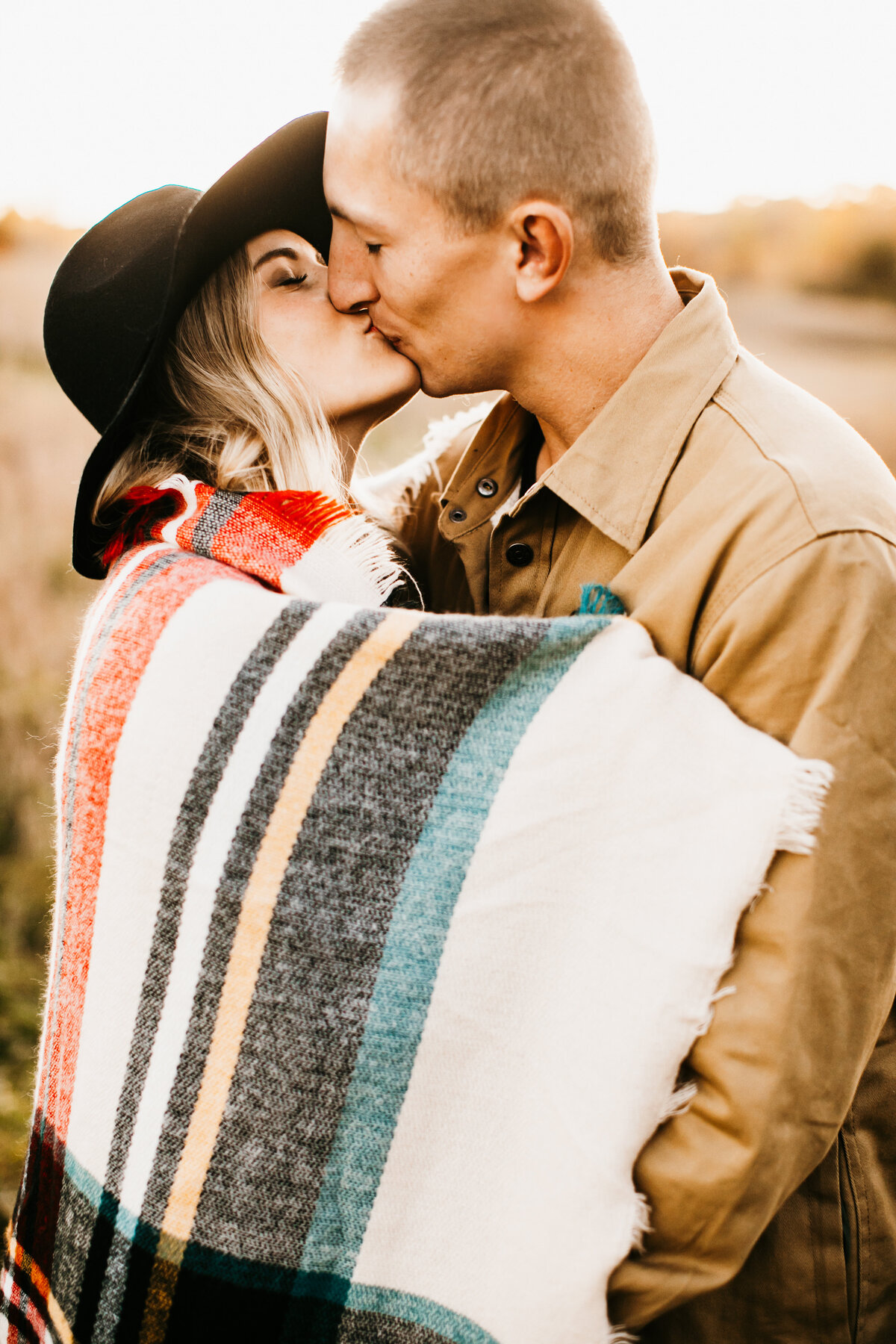 couple kissing in a field at sunset