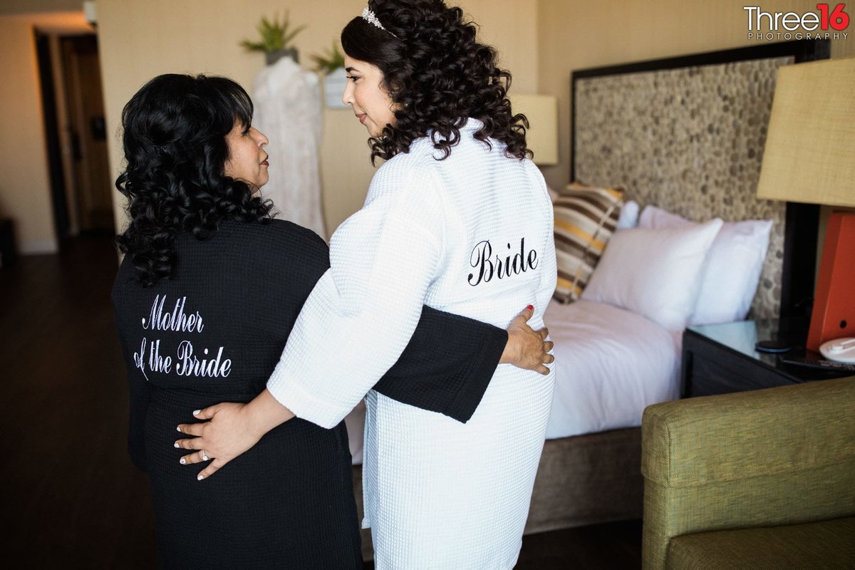 Bride posing with her mother in robes prior to getting dressed for the wedding