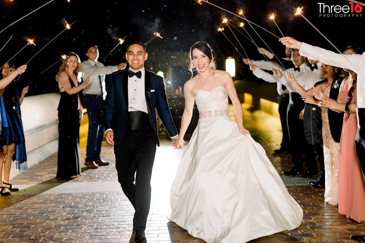 Newly married couple walks under a human tunnel of sparklers