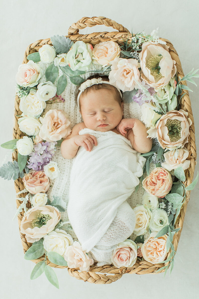 Newborn baby sleeps in a basket full of flowers in nashville newborn photographer’s studio
