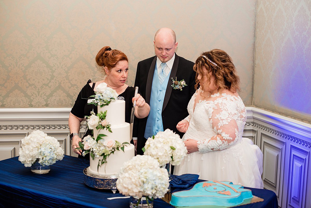 Wedding planner with Weddings & Events by Raina shows the bride and groom how to cut a wedding cake