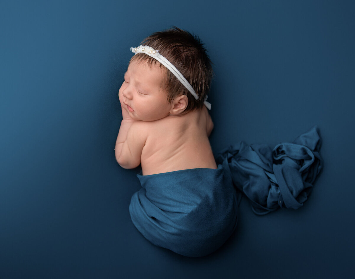 Chin on hands newborn table pose on a navy blue backdrop