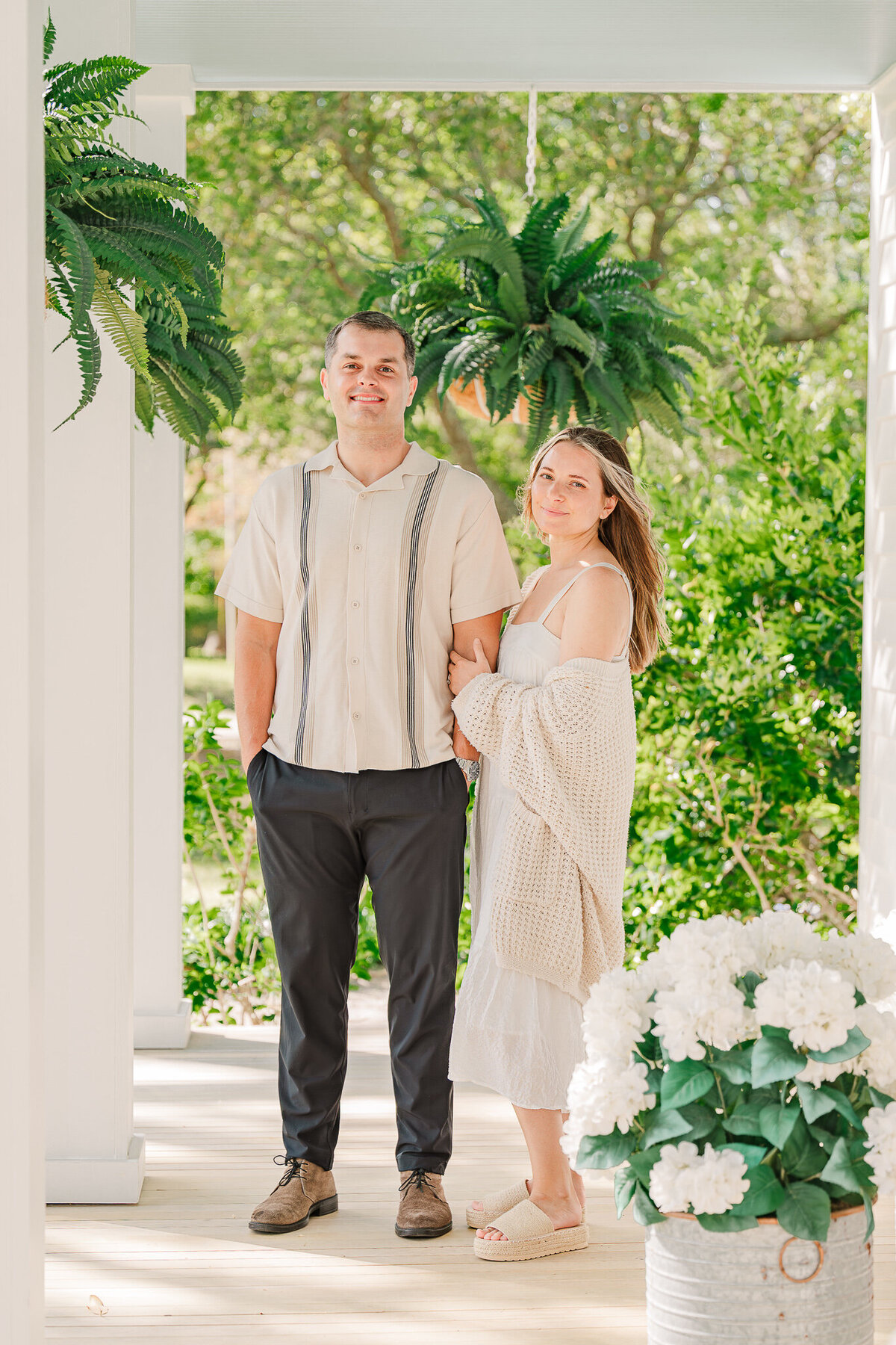 A couple locking arms during their engagement photos in the springtime surrounded by fern greenery by Raleigh wedding photographer, JoLynn Photography