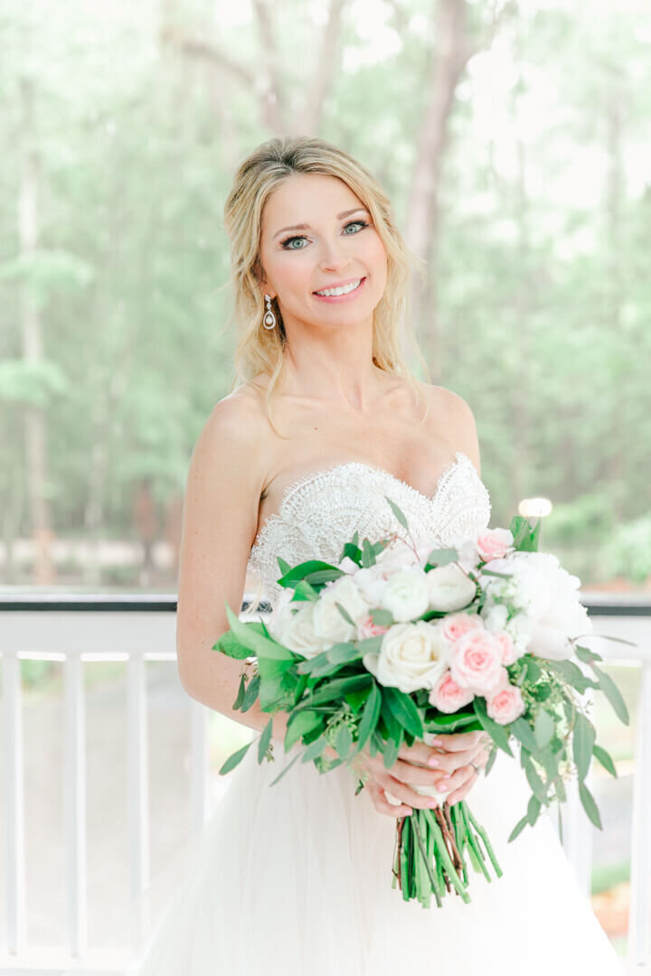 Bride stands with her green and pink bouquet for a close up portrait standing on the porch at the Mackey House captured by Arkansas Wedding photographer Photography by Karla