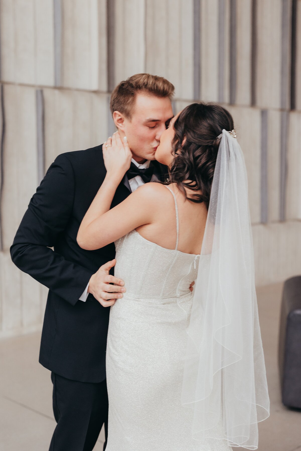A bride and groom kissing at an Iowa wedding, both dressed in bridal attire, with the bride in a white dress and the groom in a black suit.