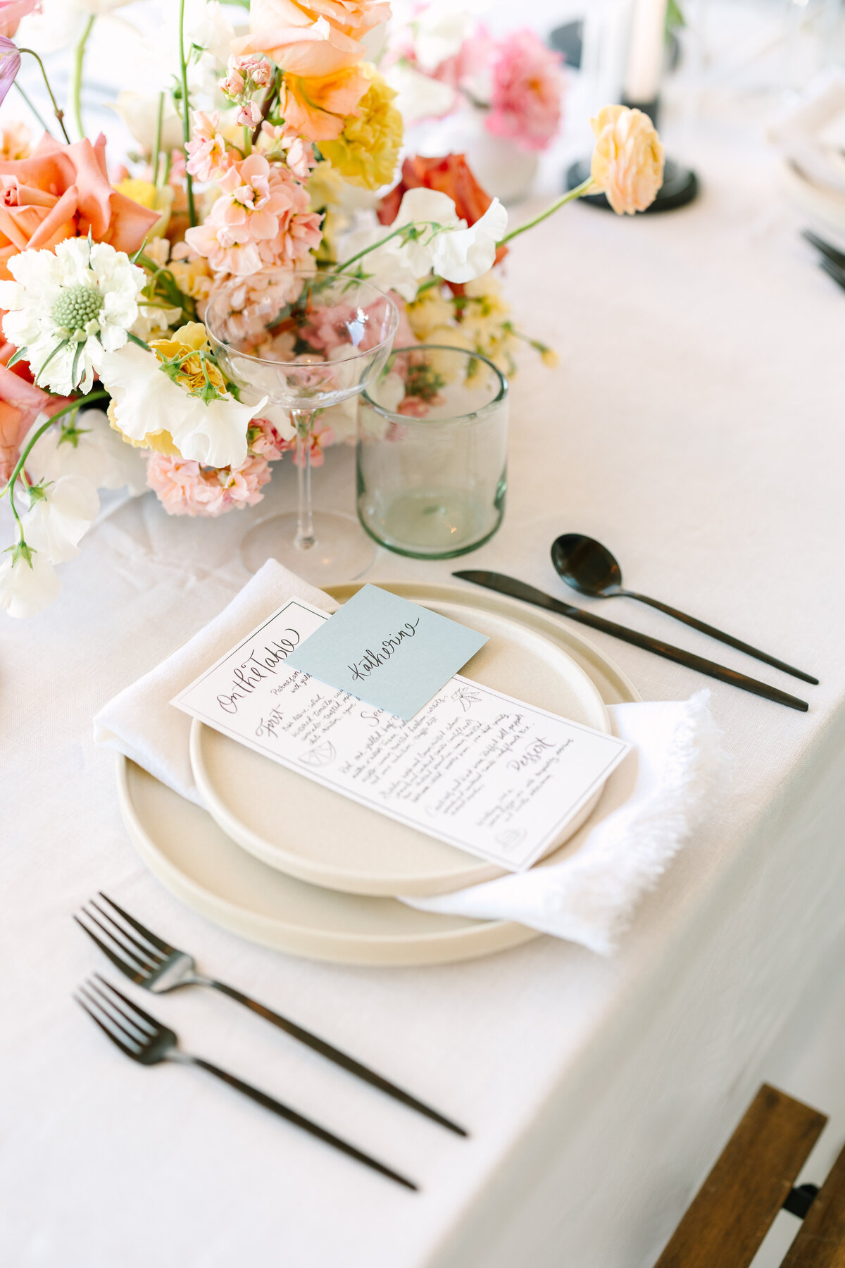wedding tablescape with dinner menu, plates, silverware, and colorful florals.