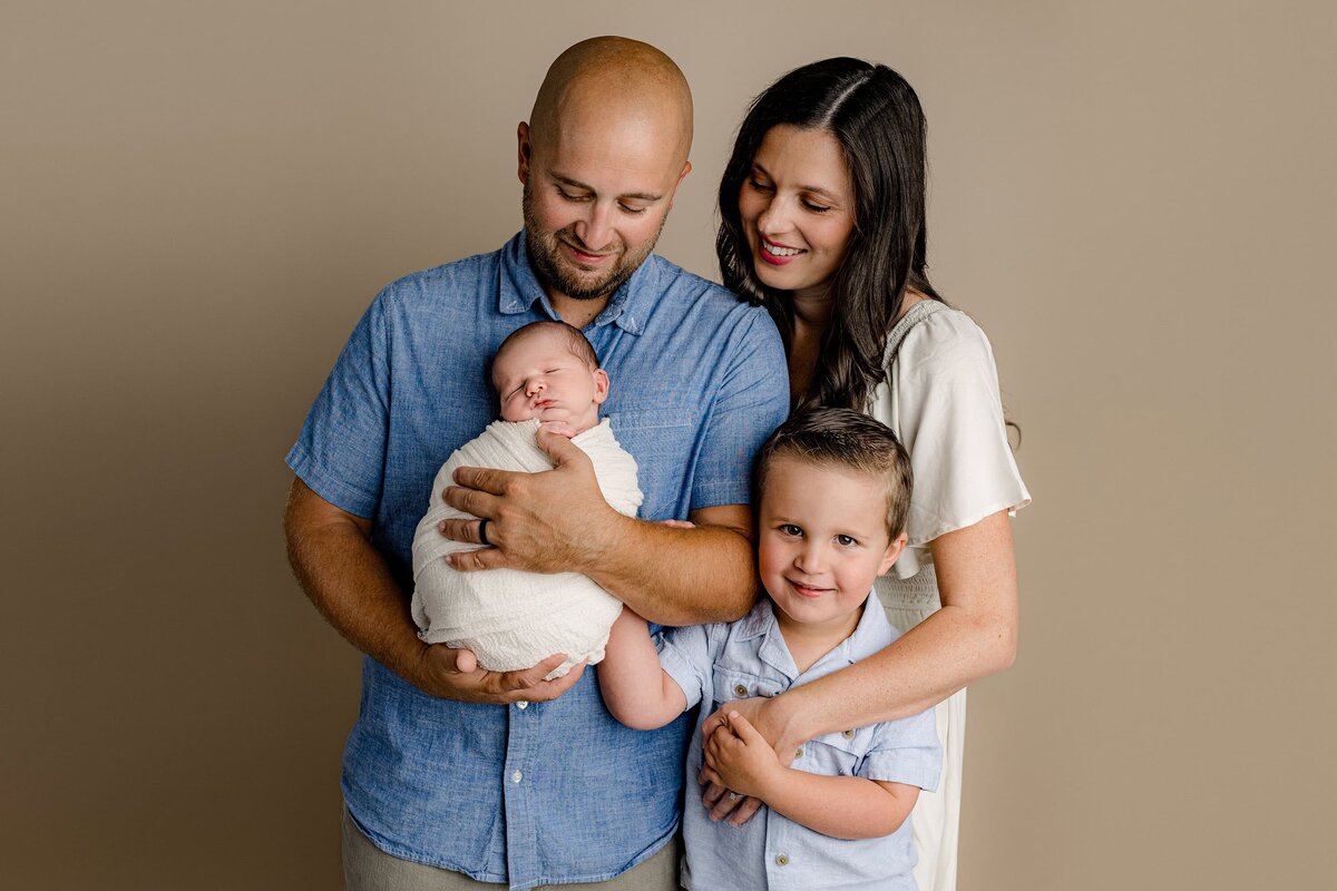 father is holding his newborn in the studio while mother and big brother stand beside him