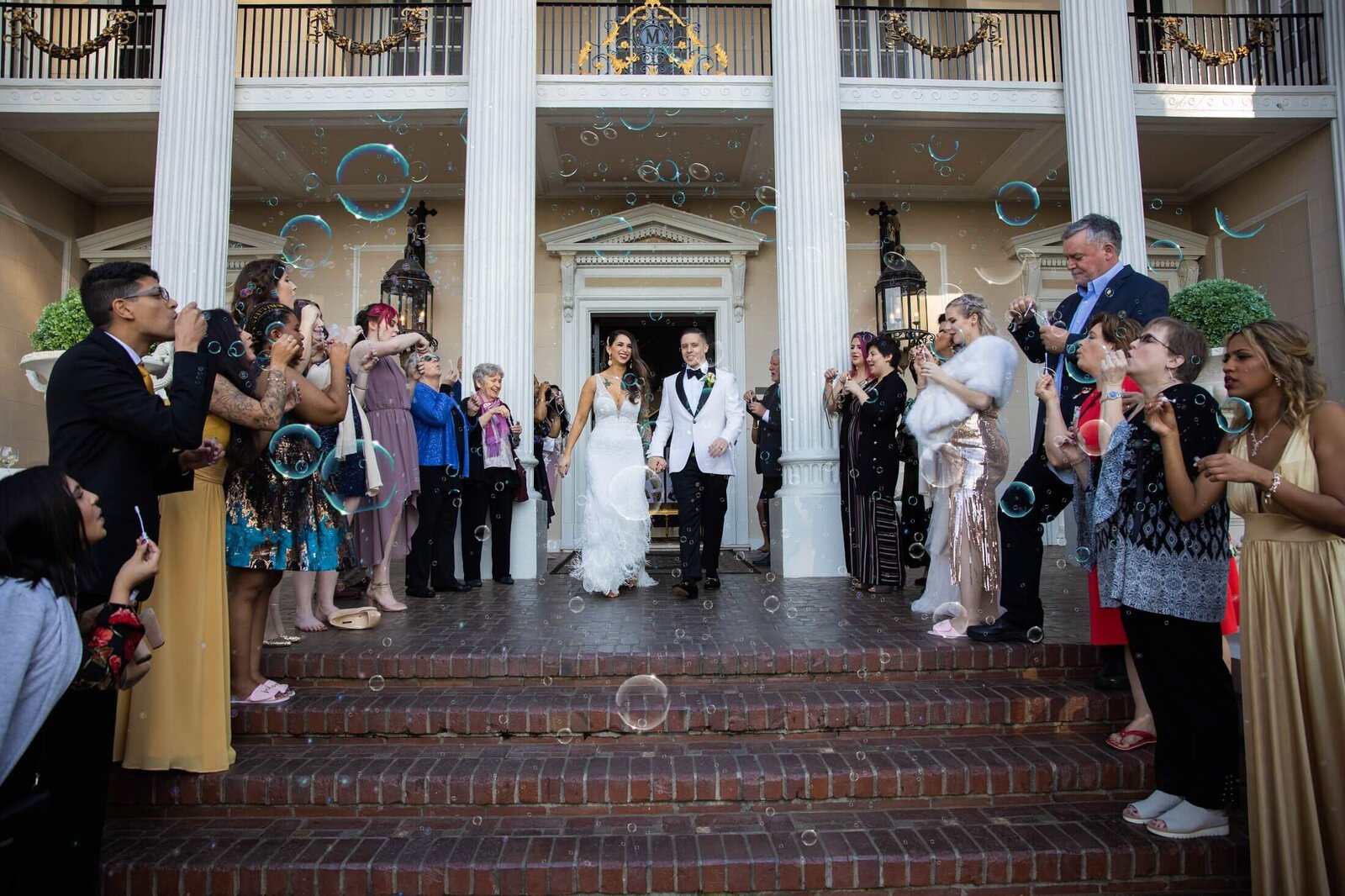 Bride and groom exit wedding reception to guests blowing bubbles on both sides at Grand Island Mansion. Captured by wedding photography studio in Sacramento, Philippe Studio Pro.