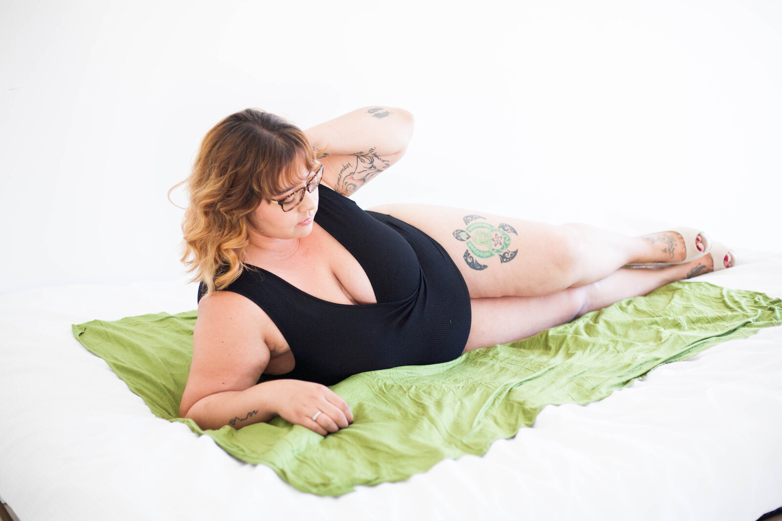 A woman in black lingerie on a green blanket in a white room.