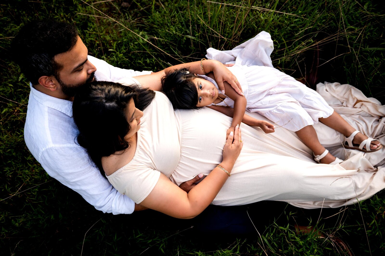 family laying in the grass as 3 year old holds her moms pregnant  belly