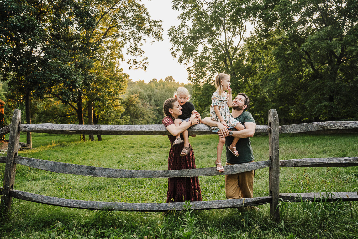 family with two kids lean against a split rail fence
