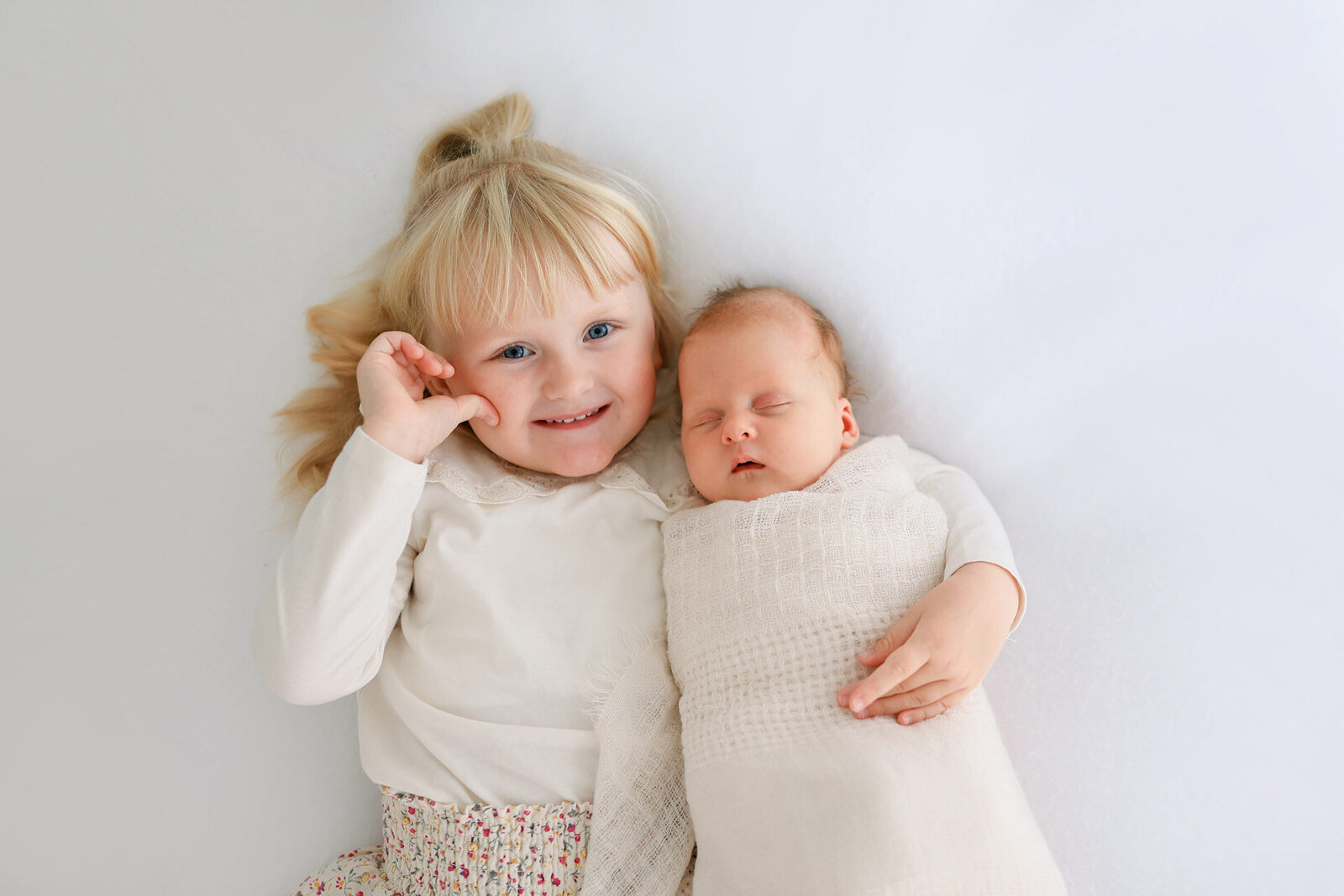 Geschwisterfotografie aus Vogelperspektive Fotoshooting bei Bielefeld: glückliches blondes Schwesterchen mit schlafendem Neugeborenen im Arm.