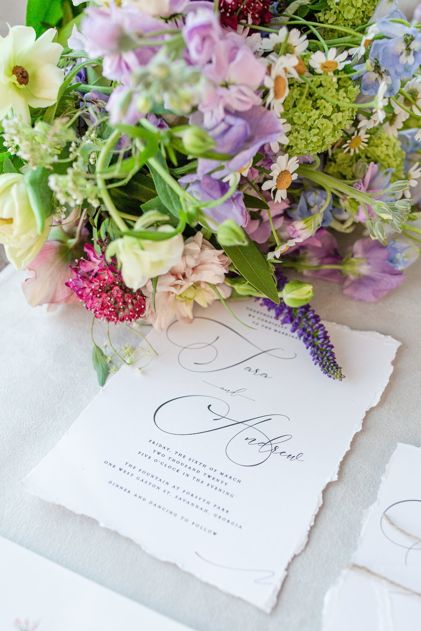 detail photo of a wedding invitation and a spring wildflower bouquet