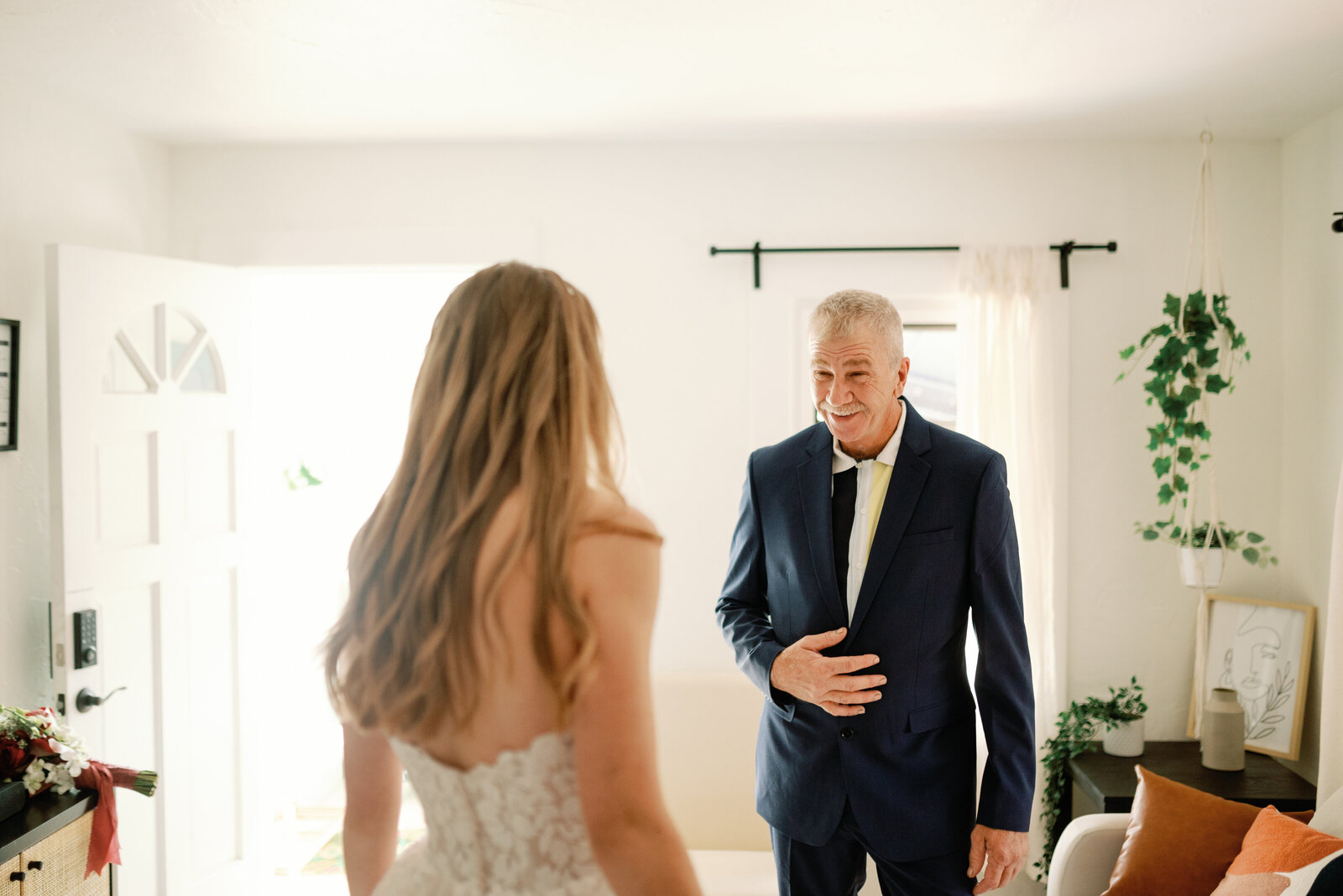 a first look with the bride and her father. Dad is smiling with his hand over his jacket buttons while looking toward his daughter in her wedding dress.