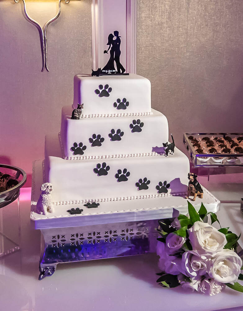a white wedding cake with black paw prints and small dog and cat figurines.