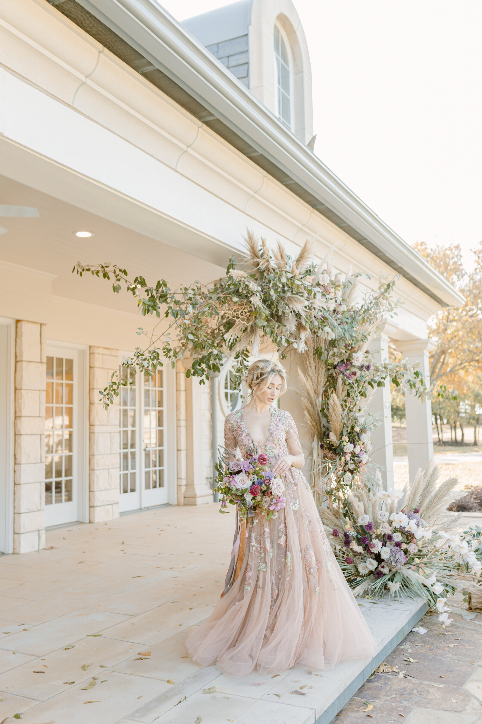 Beautiful bride outside of chateau underneath floral installation and holding a bouquet