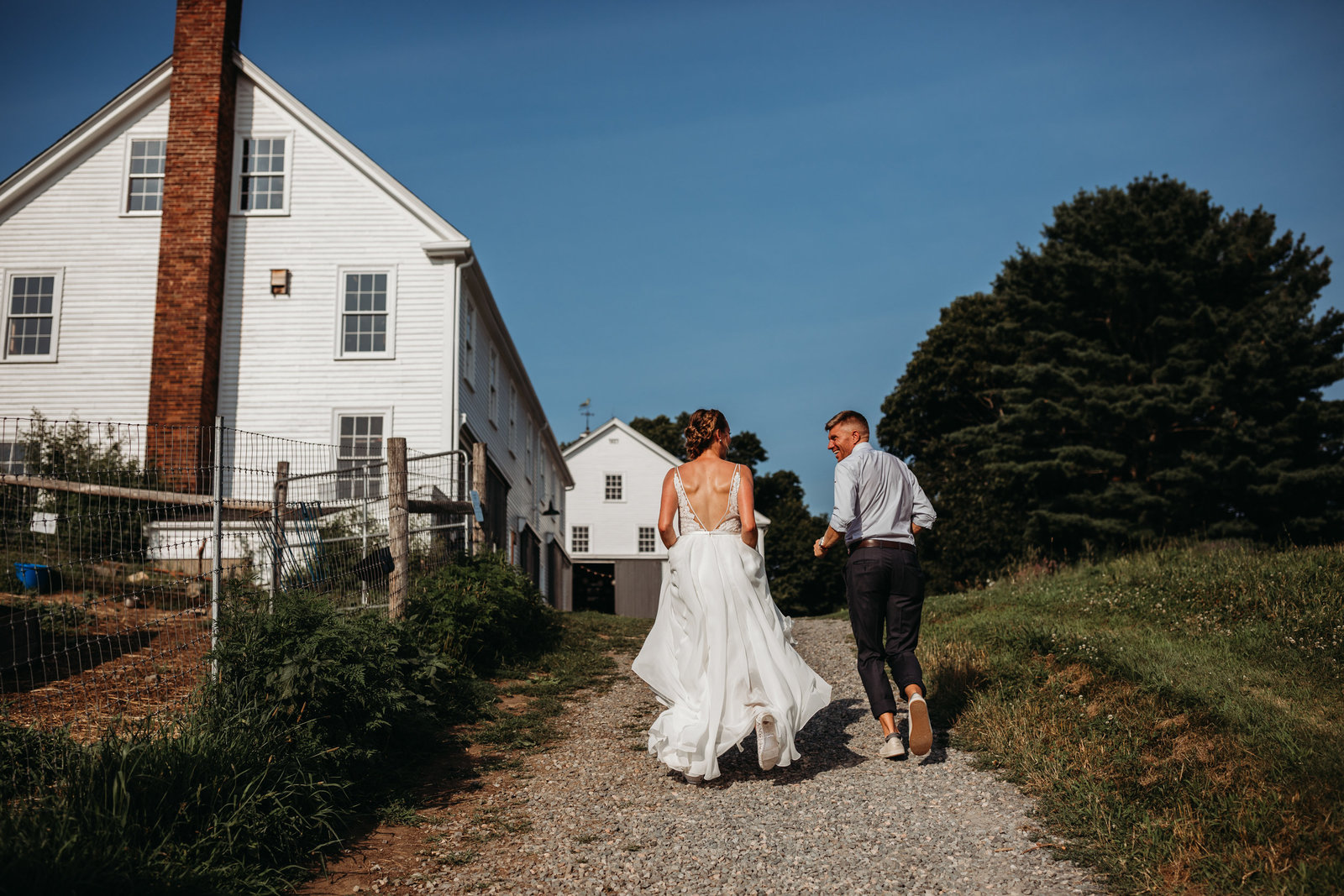 bride and groom hold hands and run past white barn