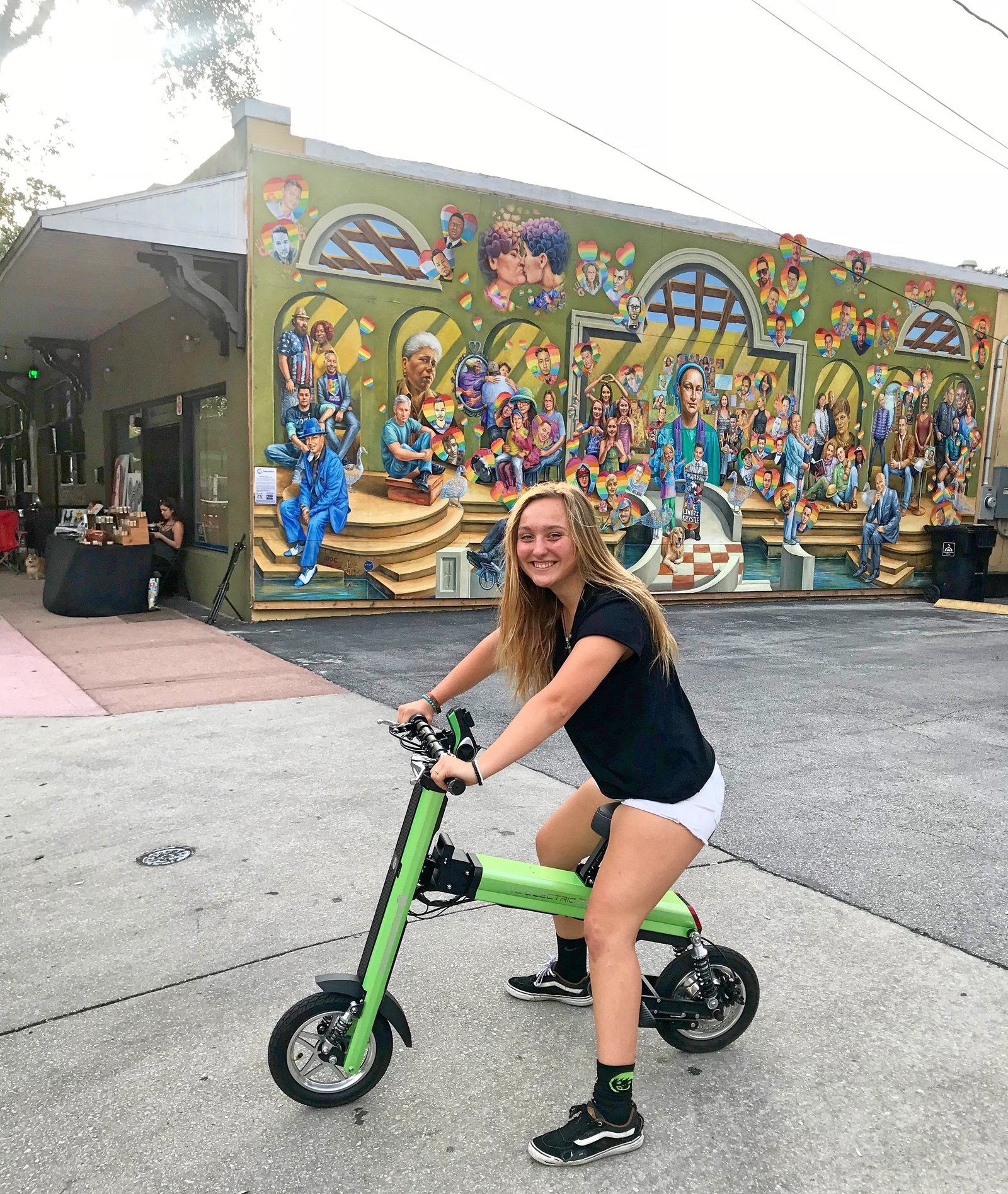 Lady on Green Go-Bike M2 with picture mural in backgrounds