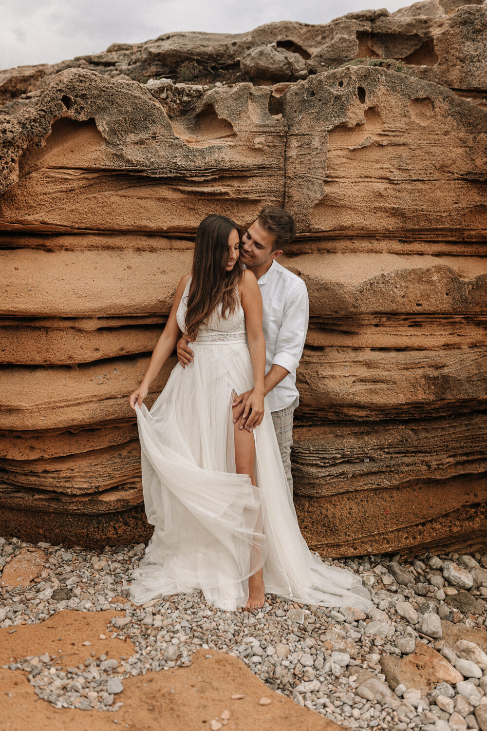Brautpaar steht vor einem Felsen an der Küste von Mallorca