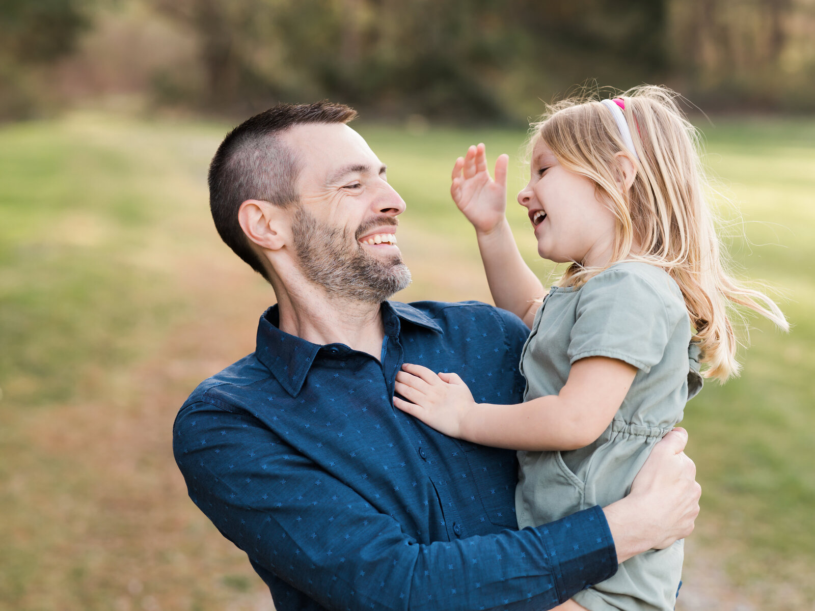 dad and daughter laughing in park for family portraits