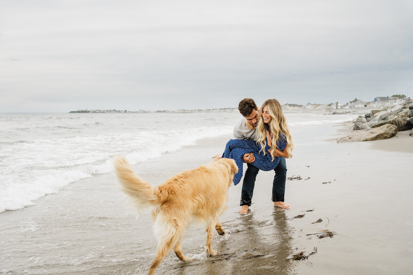 couple laughs on beach with golden retriver